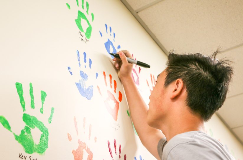 A student signing their hand print and their name on a wall.